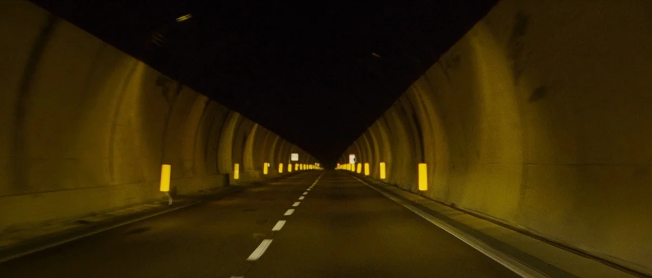 The American (2010) movie still: establishing — A long, curved concrete tunnel stretches into the darkness. Rows of yellow safety reflectors line…