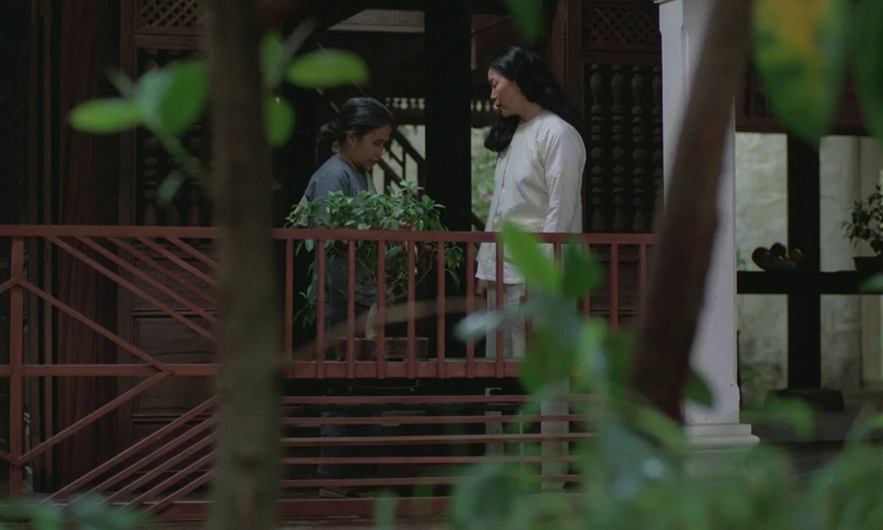 The Scent of Green Papaya (1993) movie still: medium — A wooden veranda features a red metal railing and ornate carved wood screens behind. Two…