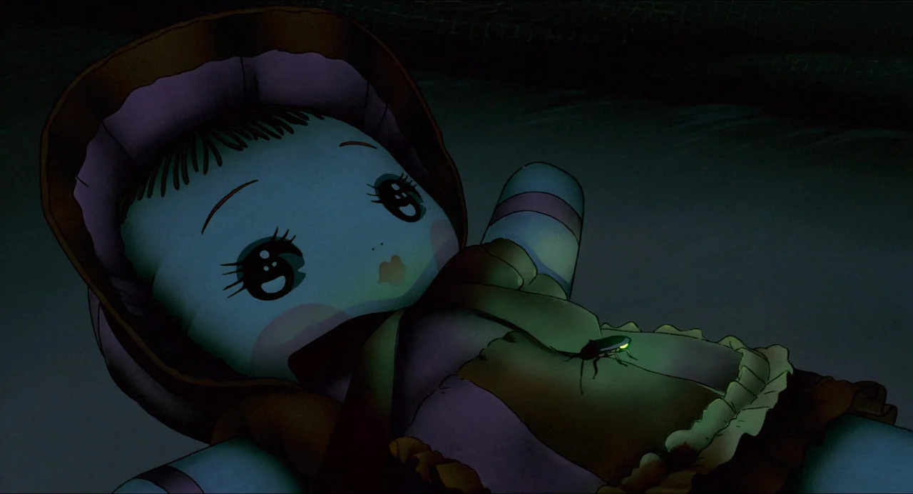 Grave of the Fireflies (1988) movie still: closeup — A doll wearing a bonnet lies on a dark, dimly lit surface. A small glowing firefly rests on the…