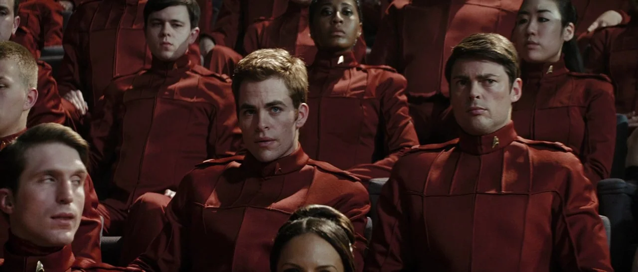 Star Trek (2009) movie still: medium — A rows of people in red military uniforms are seated in a large venue. The individuals face forward toward an…