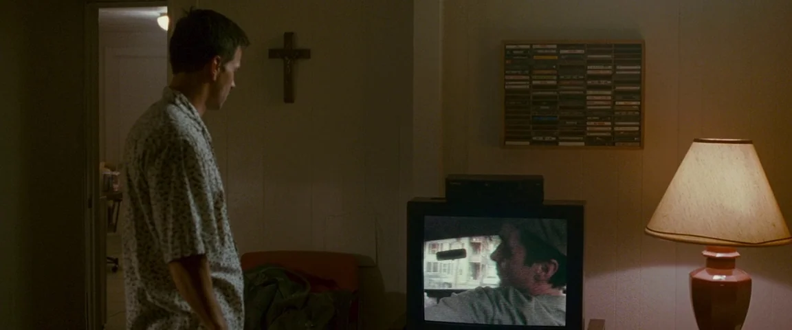 The Fighter (2010) movie still: medium — An apartment interior features a man standing before a television displaying a recorded image. A…