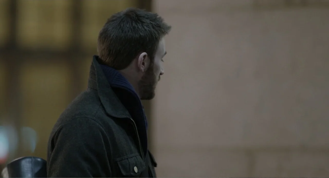 Before We Go (2014) movie still: medium — An interior space features a smooth wall and blurred background elements. A man wearing a dark jacket…
