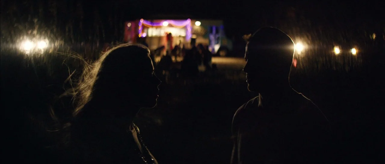 Magic Mike XXL (2015) movie still: medium — Two individuals stand in a dark, open area facing each other in silhouette. A vehicle with bright…