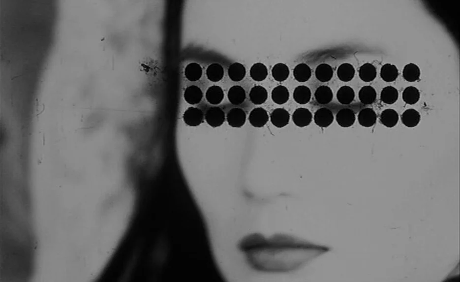 Irma Vep (1996) movie still: closeup — A close-up of a human face features a black bar over the eye area. The black bar consists of three rows of…