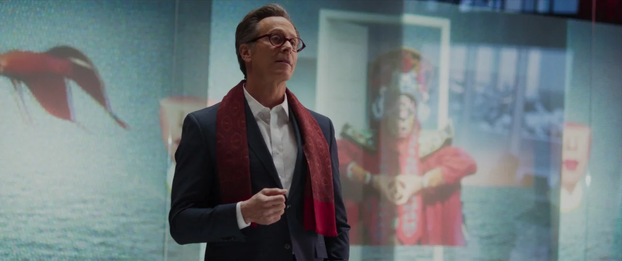 The Perfection (2018) movie still: medium — A man stands in front of massive digital displays showing video of fish and performers. He is centered…