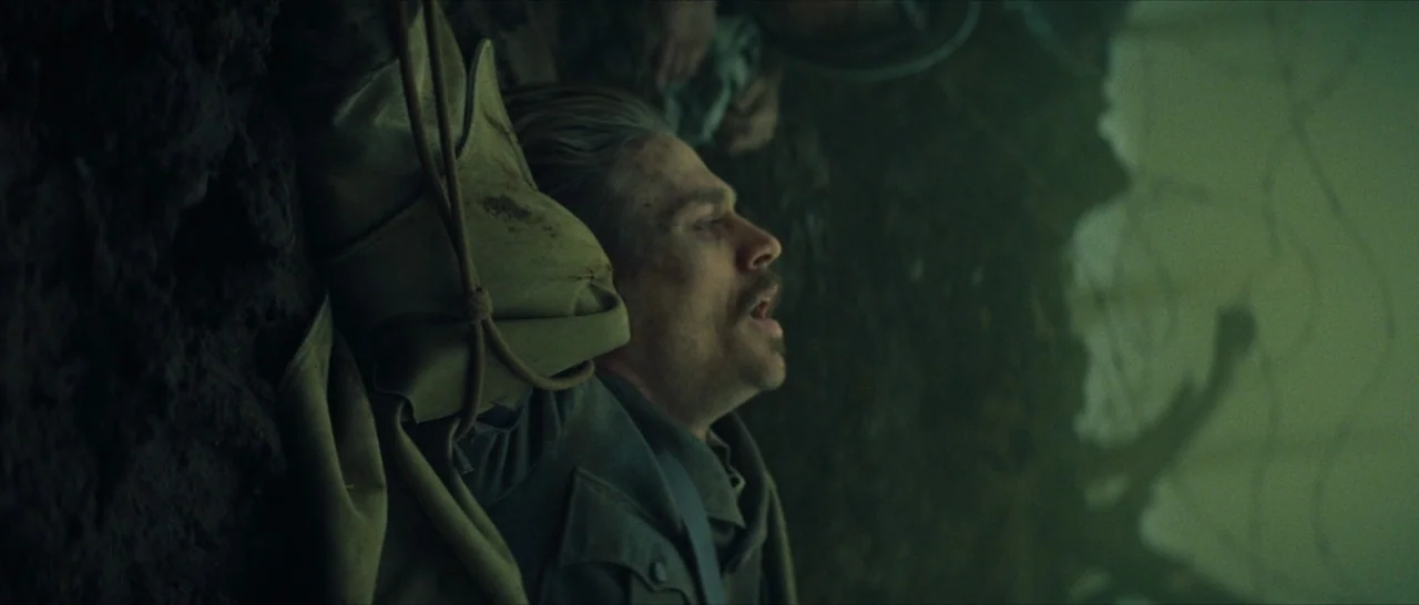 The Lost City of Z (2016) movie still: closeup — A dark muddy trench with a soldier lying on the uneven ground. The man is gasping for air while…