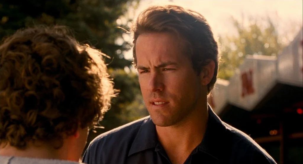 Adventureland (2009) movie still: medium — An outdoor area with foliage in the background under bright daylight. A man speaks to another individual…