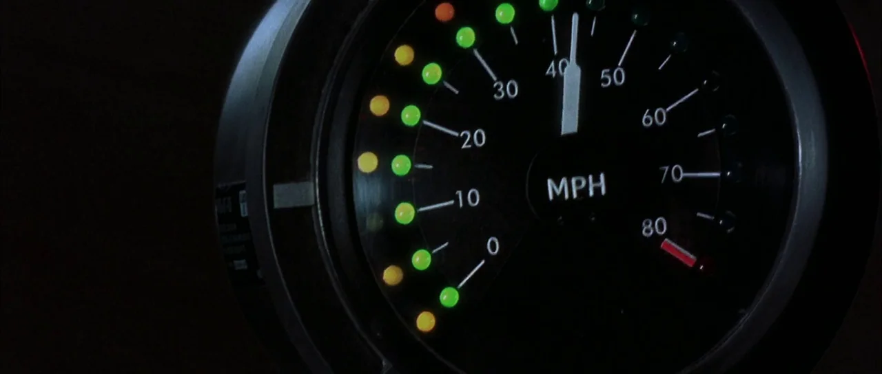 The World is Not Enough (1999) movie still: closeup — A circular speedometer gauge features bright LED-style indicators in green and amber. The…