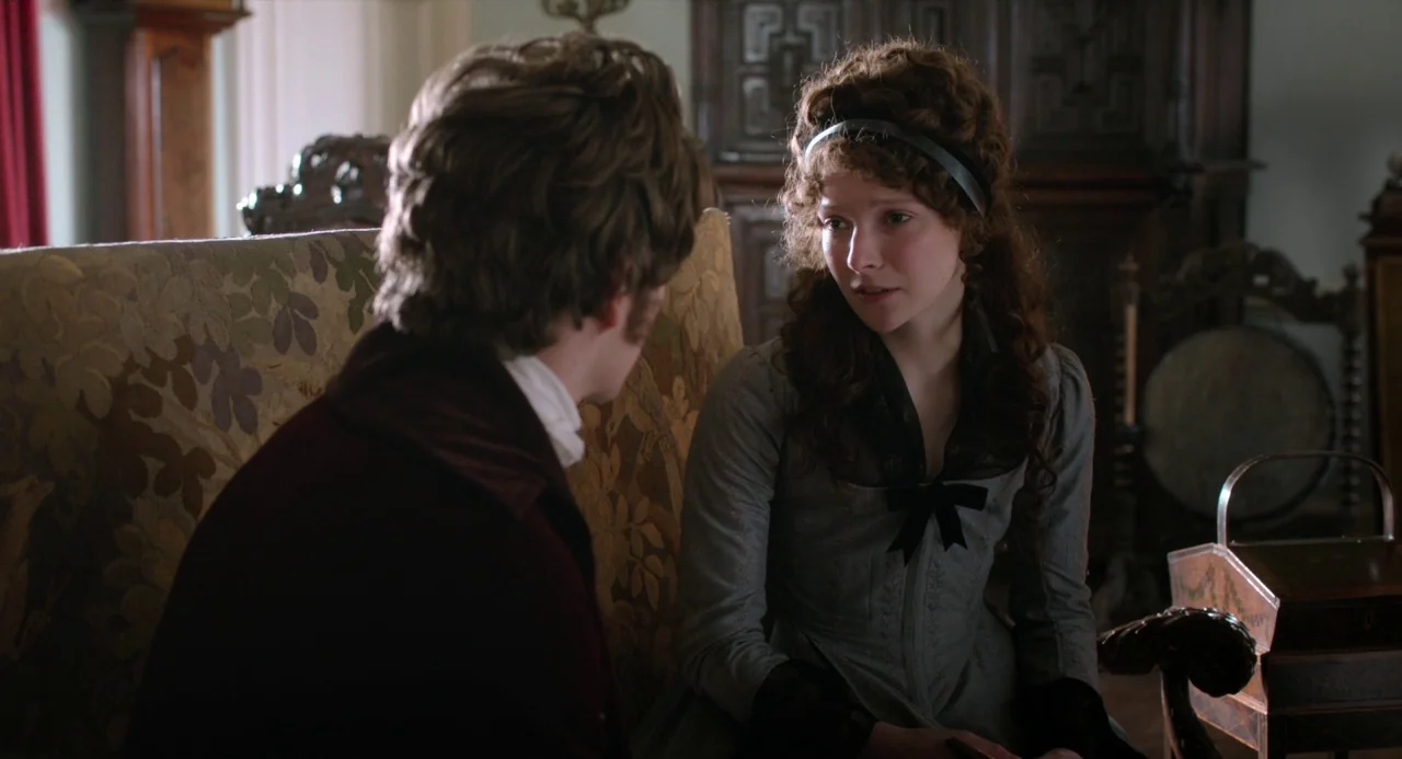 Love and Friendship (2016) movie still: medium — A 19th-century interior with period furniture including a patterned fabric sofa and wooden cabinet.…