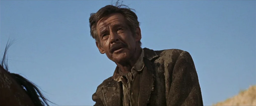The Wild Bunch (1969) movie still: medium — A man rides through an open landscape under a clear, bright blue sky. The man wears a grit-covered, worn…