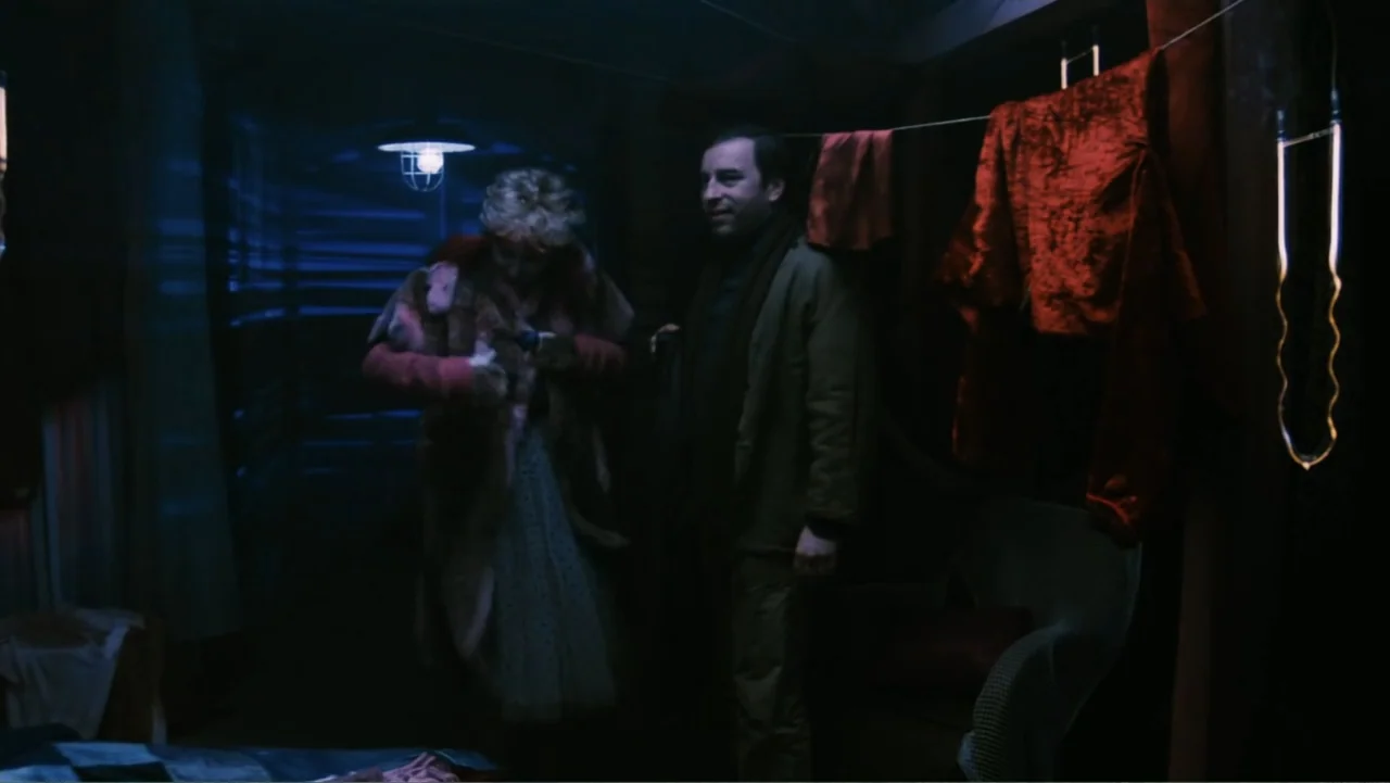 O-Bi, O-Ba: The End of Civilization (1985) movie still: medium — A dimly lit room contains two people standing near hanging red fabric and clothing.…