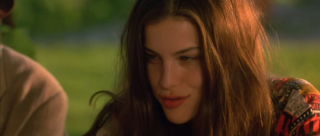 Stealing Beauty (1996) movie still: closeup — A young woman stands outdoors in a grassy field during the late afternoon. She looks down while…