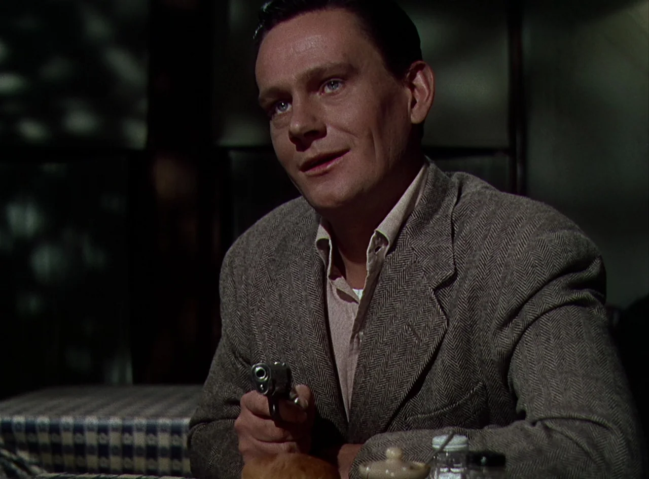 Desert Fury (1947) movie still: medium — A man sits in a diner booth with patterned upholstery and a condiment set nearby. The man holds a revolver…