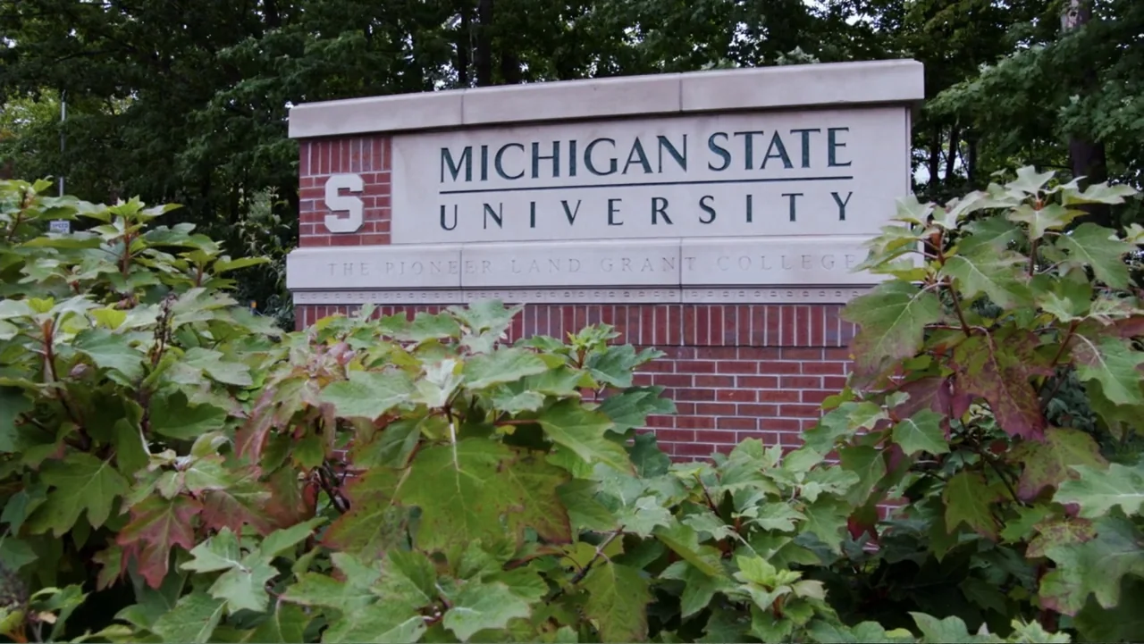 At the Heart of Gold: Inside the USA Gymnastics Scandal (2019) movie still: medium — A brick and stone monument sign for Michigan State University…