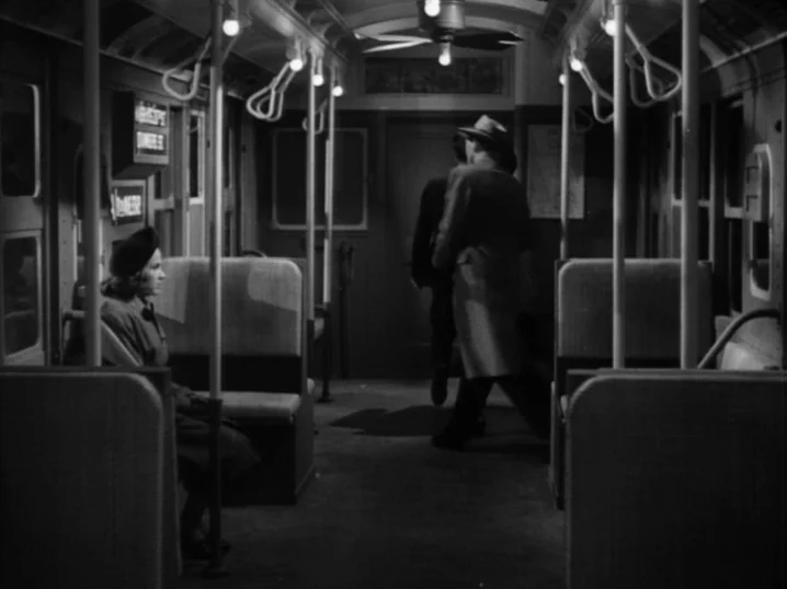 The Seventh Victim (1943) movie still: wide — A dimly lit subway car interior features rows of padded bench seats and overhead grab-handles. A lone…