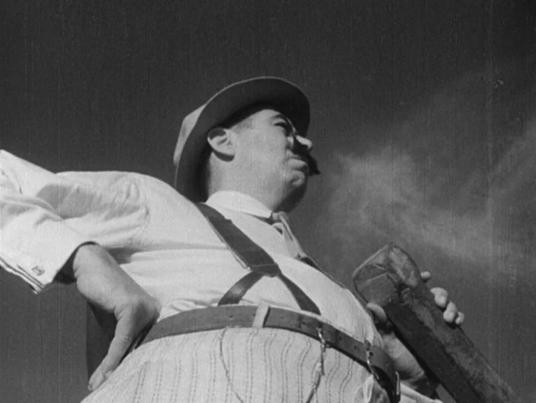 Redes (1936) movie still: medium — A man wearing a hat and suspenders stands outside against an overcast sky. He holds a rectangular wooden object…