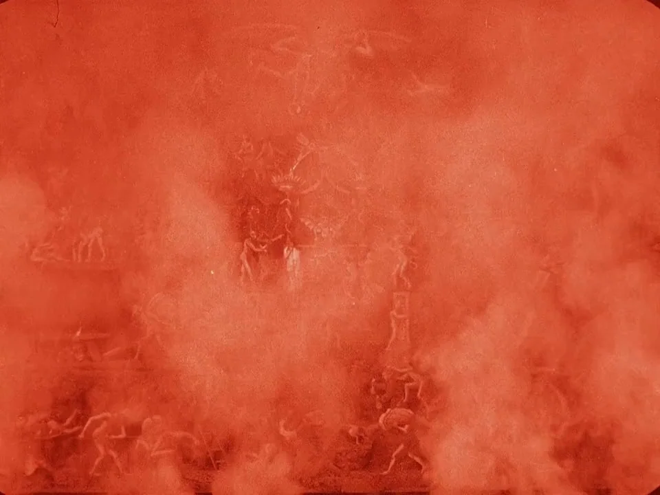 Häxan (1922) movie still: establishing — A theatrical stage set features numerous small figures arranged in a dense, smoky environment. The actors…