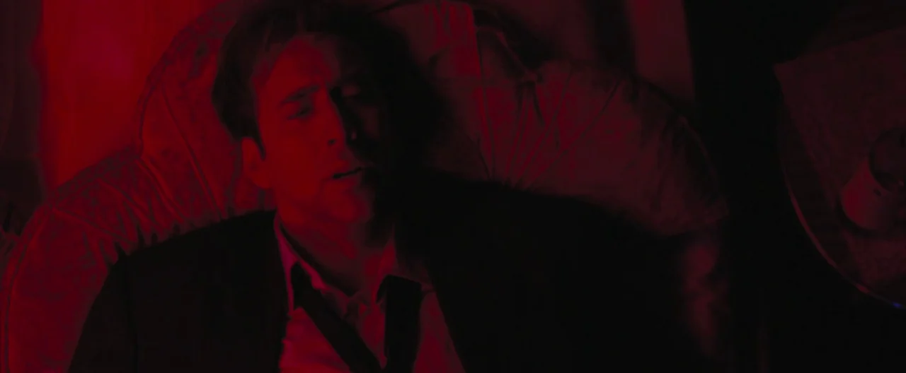 Lord of War (2005) movie still: closeup — A man lies on a plush sofa illuminated by an intense red light source. He rests with his eyes closed while…