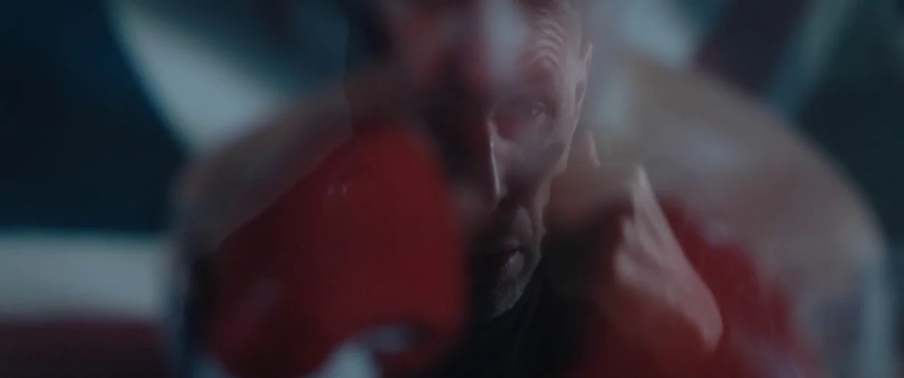 Journeyman (2017) movie still: closeup — A blurry close-up of a boxer in a dark space during a training session. The subject punches directly toward…