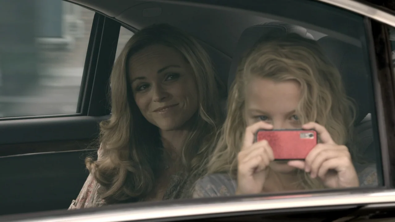 6 Bullets (2012) movie still: medium — The interior of a moving car with a woman and child sitting together. The woman looks at the child who is…