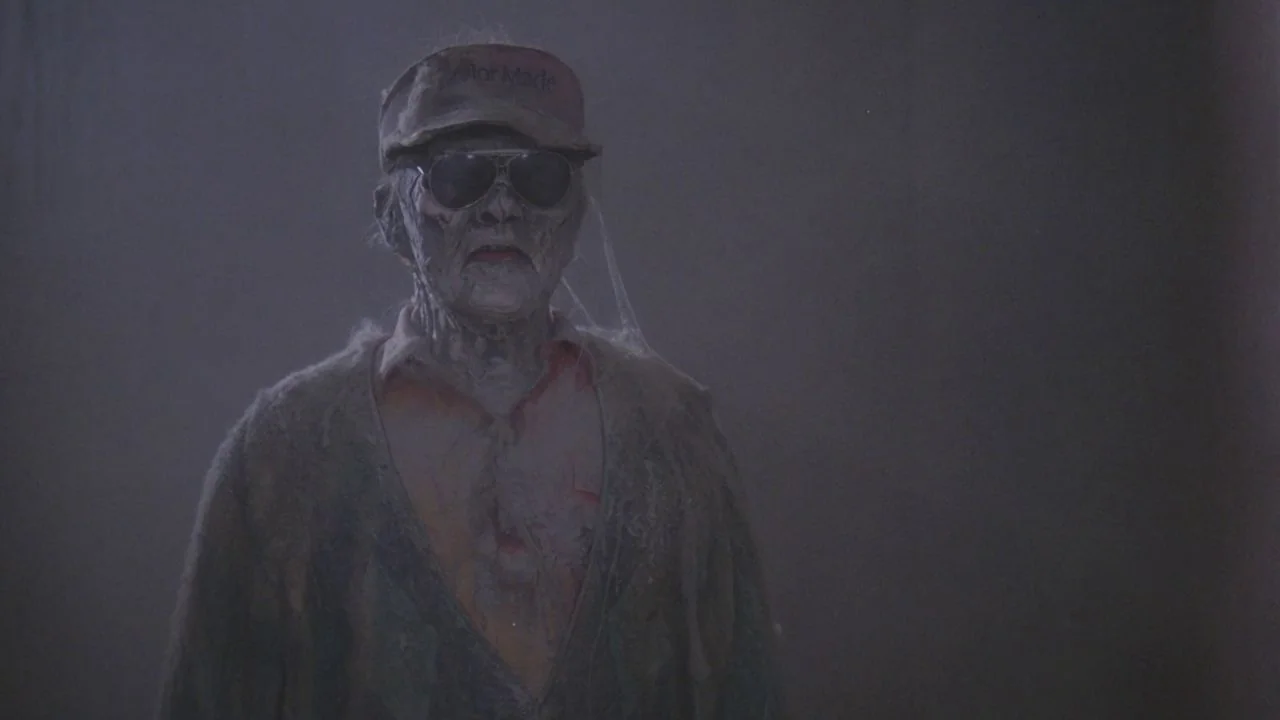 Scrooged (1988) movie still: medium — A dark, indistinct indoor space with hazy, low-contrast atmosphere. An elderly male figure with decaying…
