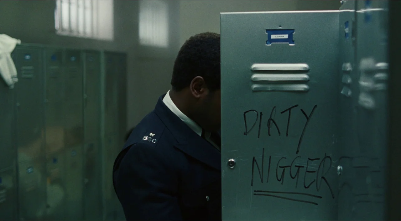Red, White & Blue (2020) movie still: medium — An interior space features rows of industrial metal lockers painted a dull grey color. A black man in…