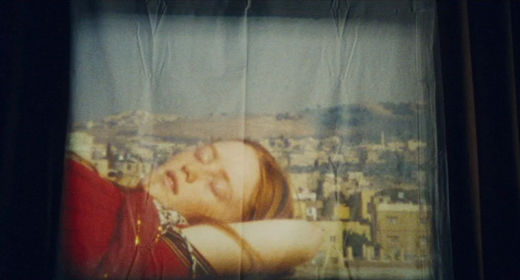 Something in the Air (2012) movie still: closeup — A projection of a young woman sleeping appears on a wrinkled, translucent fabric screen. The…