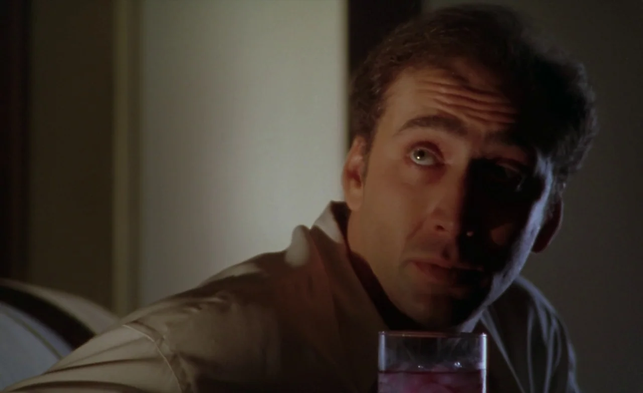 Leaving Las Vegas (1995) movie still: closeup — A man in a button-down shirt sits in a dimly lit room at night. He holds a glass while looking…