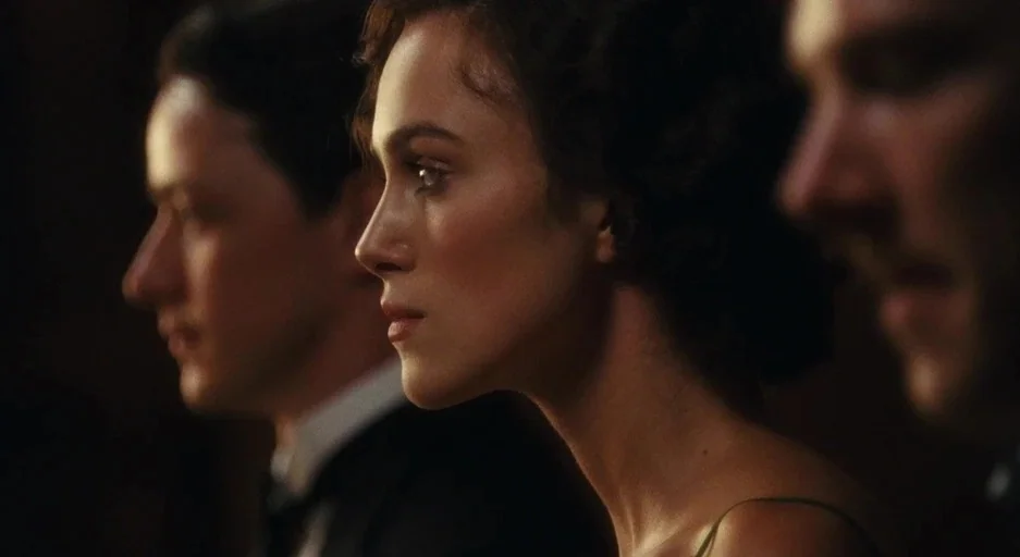 Atonement (2007) movie still: medium — A dimly lit room with a brown, nondescript background focused on several seated individuals. The figures are…