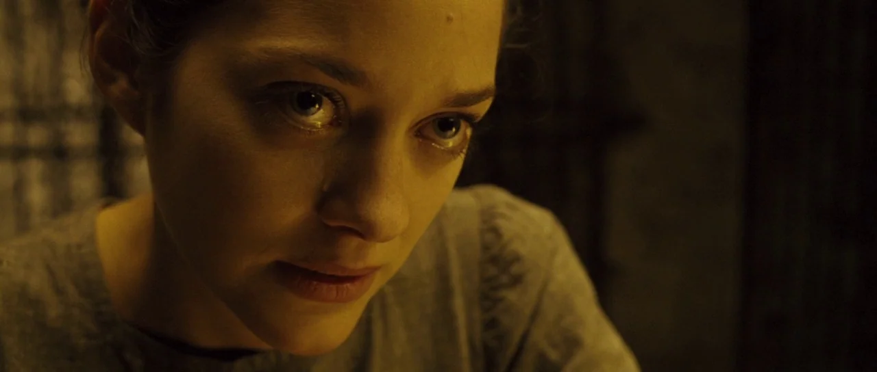 A Very Long Engagement (2004) movie still: closeup — A dimly lit room with dark, obscured textures in the background. A woman with a tear on her…