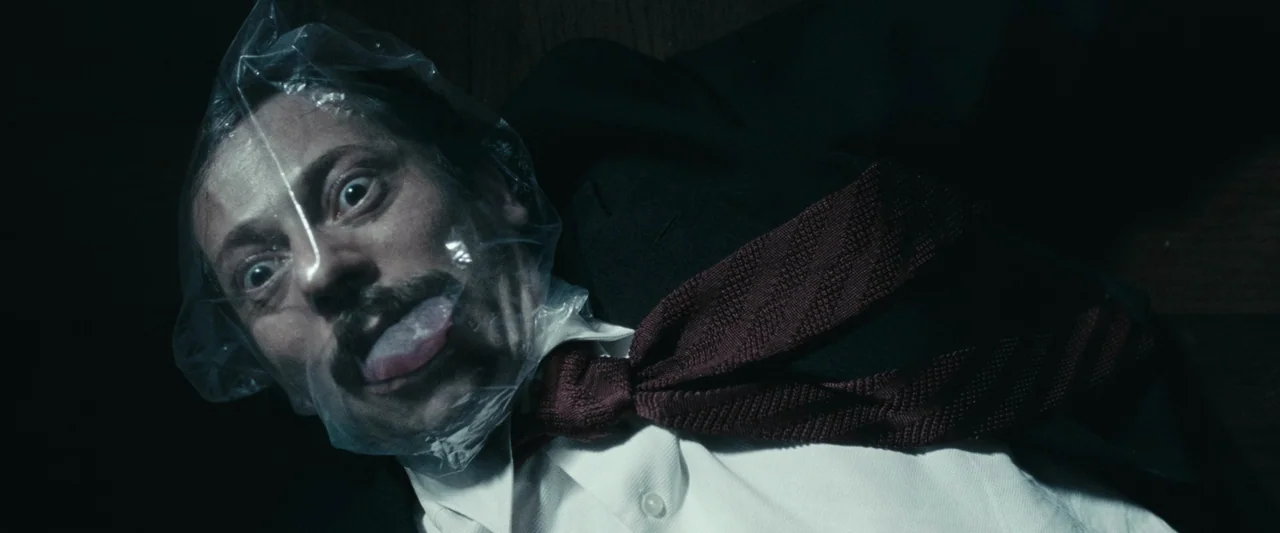 Chicken With Plums (2011) movie still: closeup — A man with a plastic bag secured around his head lies flat on dark wood. His eyes are wide as he…
