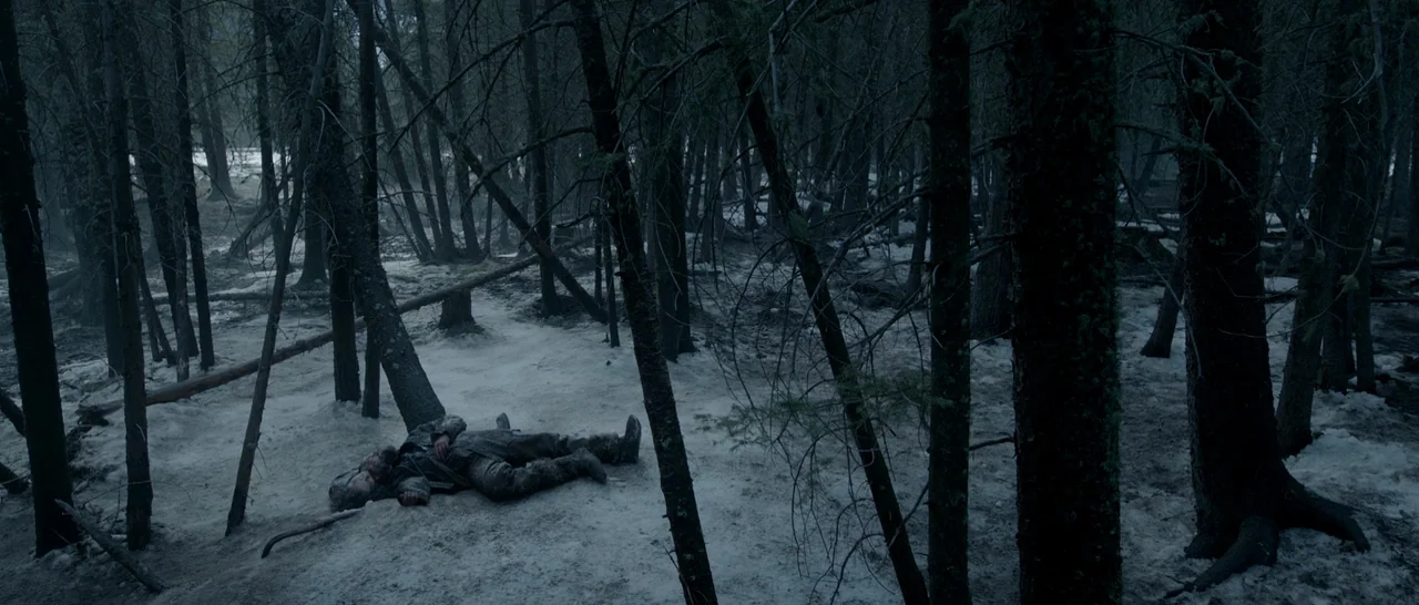The Revenant (2015) movie still: wide — A dense, cold woodland is covered in a patchy layer of melting winter snow. A man lies flat on his back on…