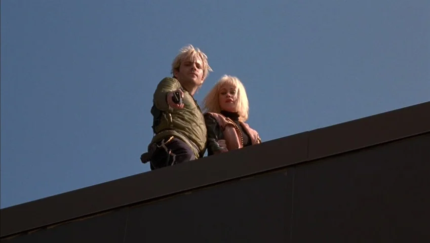 Making of: Castle Freak (1995) movie still: medium — A man and a woman stand on the flat edge of a building against blue sky. The man holds a…