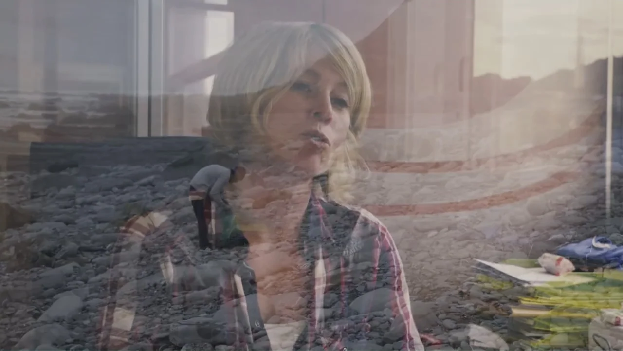 Hondar 2050 (2018) movie still: medium — A woman is superimposed over a double-exposed view of a rocky shoreline. A person walks along the beach…