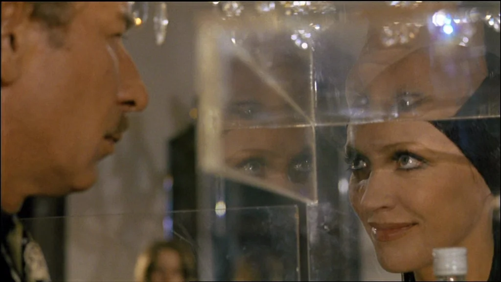 Chinese Roulette (1976) movie still: closeup — A man and a woman face each other behind a clear glass partition. The setting contains visible…
