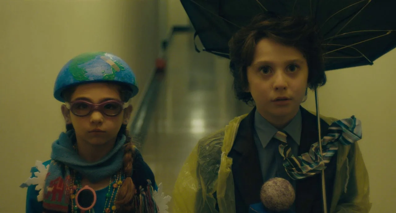 Private Life (2018) movie still: medium — A quiet and sterile building corridor with light-colored walls and fluorescent lighting. A boy with a…
