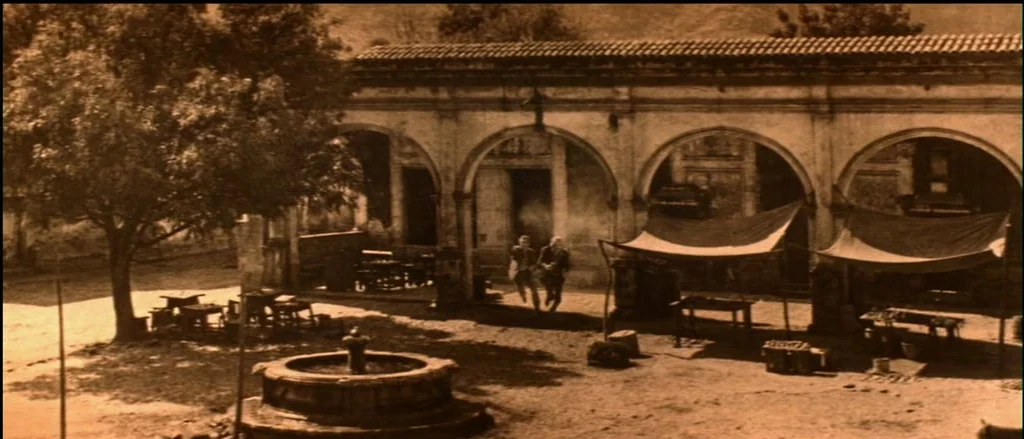 Butch Cassidy and the Sundance Kid (1969) movie still: wide — A stone courtyard features a central circular fountain and arched colonnade with…