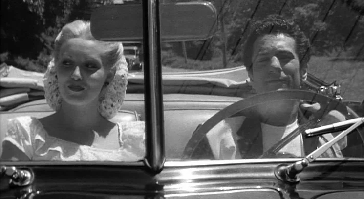 Raging Bull (1980) movie still: medium — A vintage convertible car travels along a sunlit road bordered by trees. A man drives while a blonde woman…