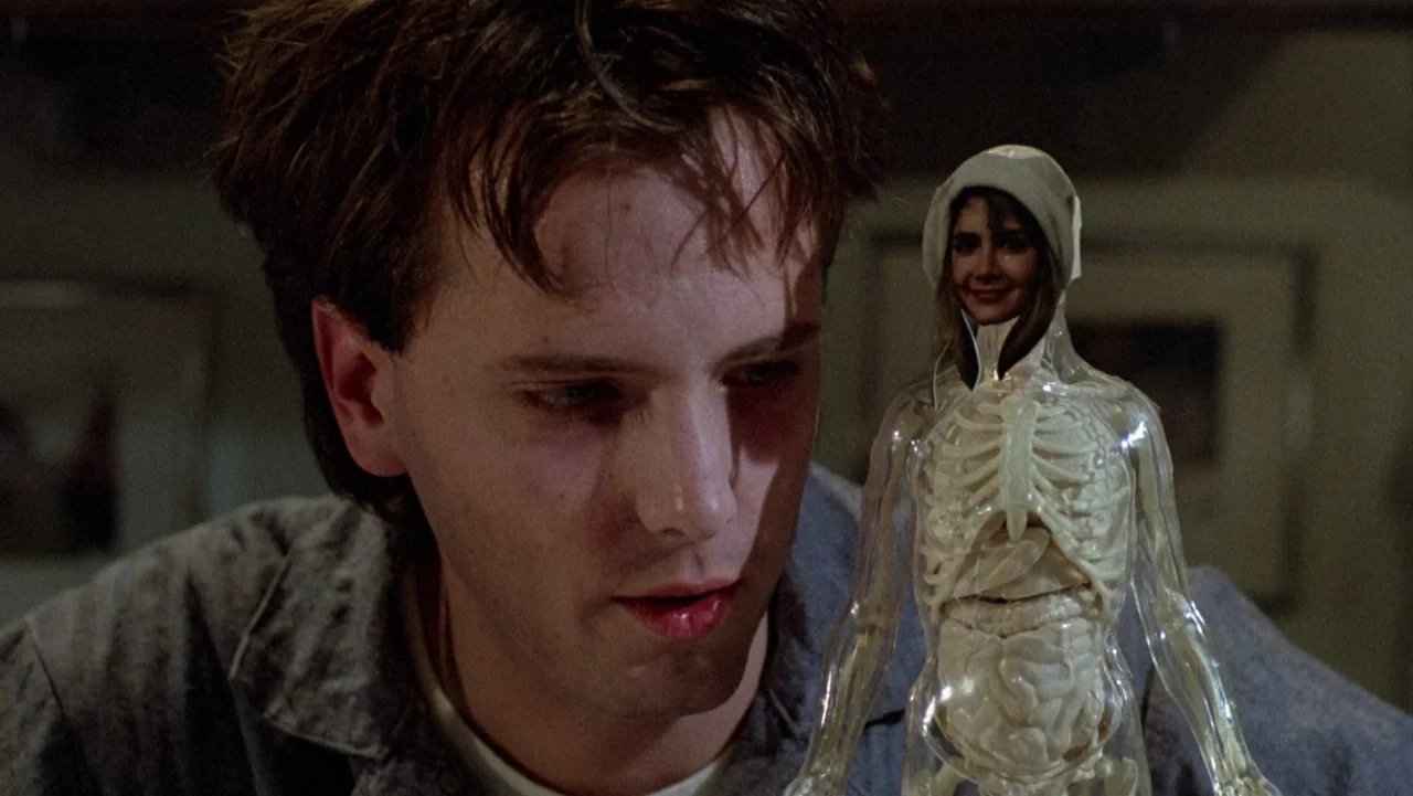 Frankenhooker (1990) movie still: medium — A dimly lit room serves as the setting for a quiet, focused observation. A young man stares intently at a…