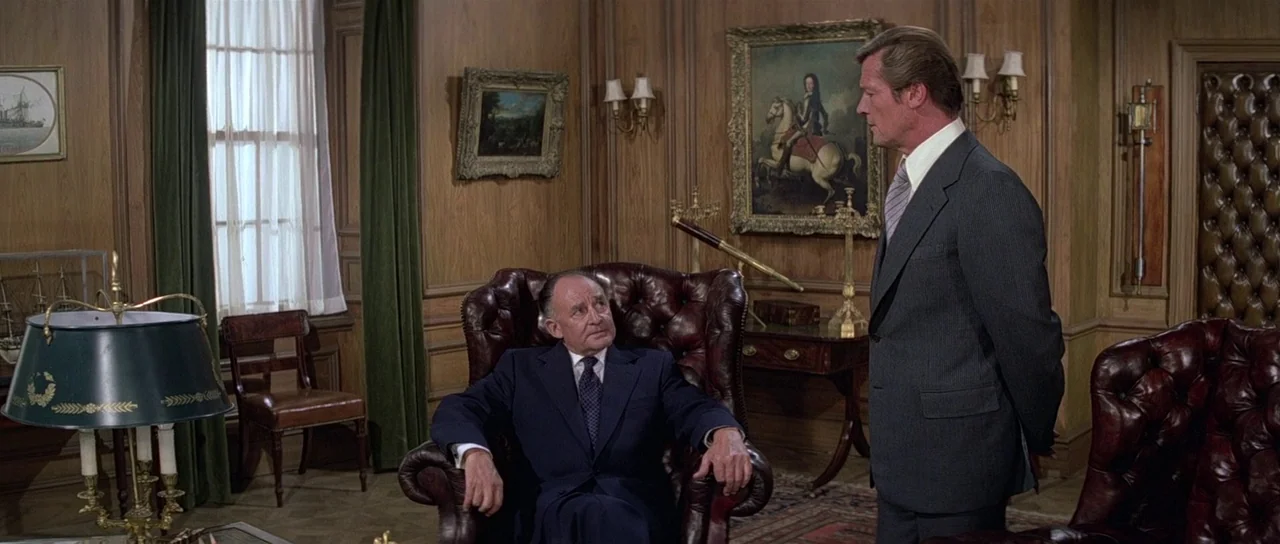 Moonraker (1979) movie still: medium — A wood-paneled room features leather armchairs, oil paintings, and a telescope on a table. One man stands…