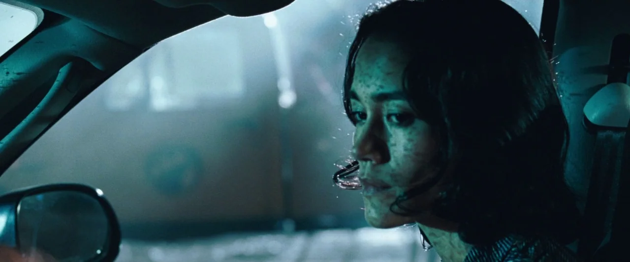 Resident Evil: Apocalypse (2004) movie still: closeup — A dark, cramped interior of a vehicle at night with blue ambient lighting. A woman sits in…