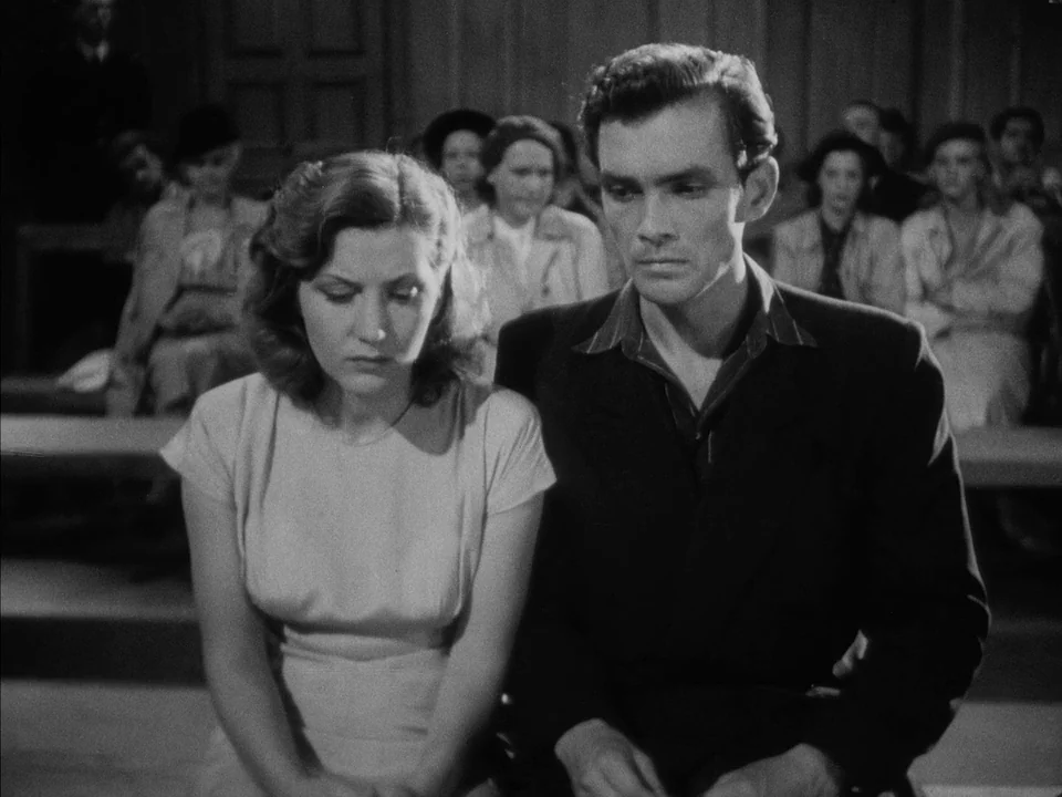 It Rains On Our Love (1946) movie still: medium — A crowded wooden bench in a public viewing gallery with blurred people in back. A man and a woman…
