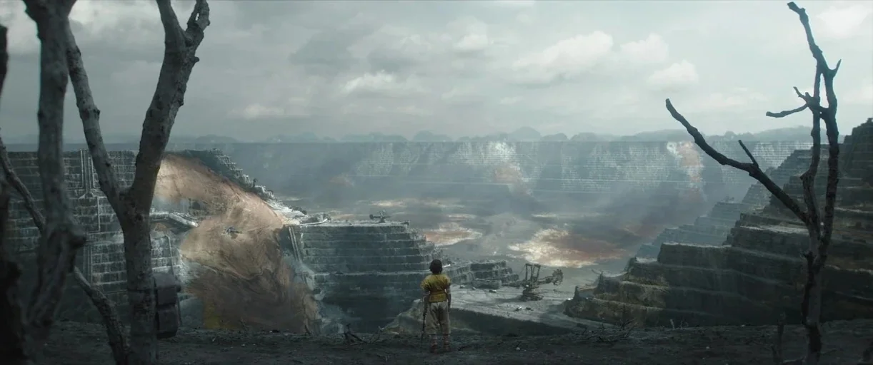 Andor (2022) movie still: wide — A vast, multi-tiered open-pit mine stretches into the distant horizon under a cloudy sky. A solitary child stands…