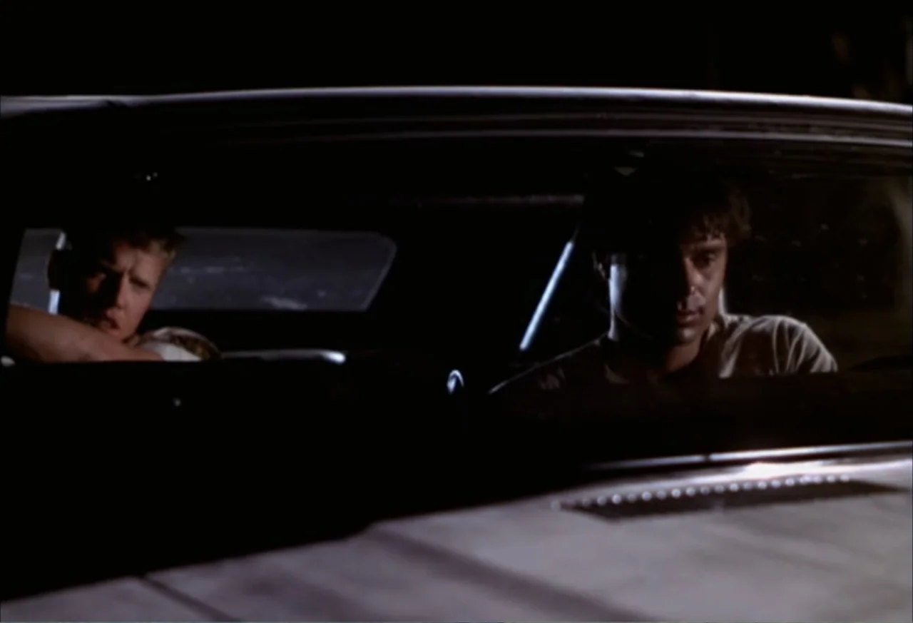 Black Cat Run (1998) movie still: medium — The interior of a car at night serves as the setting for two passengers. Two men sit in the front seats…