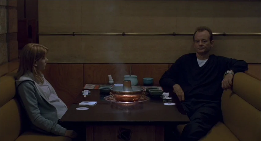 Lost In Translation (2003) movie still: medium — A dimly lit restaurant booth features wood paneling and a dark, polished table. A woman and a man…