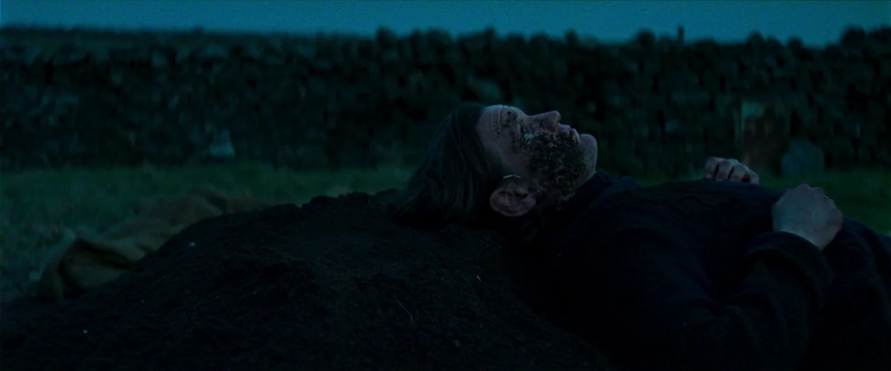 Starve Acre (2023) movie still: medium — An open rural landscape at night features a dry-stone wall in the background. A man lies still on a mound…