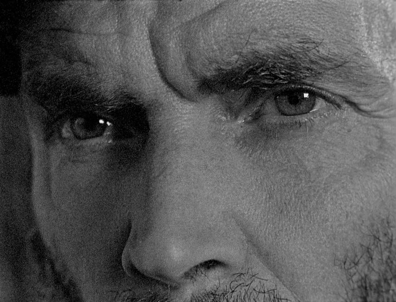 Bait (2019) movie still: closeup — An extremely close-up view of a man's eyes and upper face features. The image focuses on skin texture and facial…