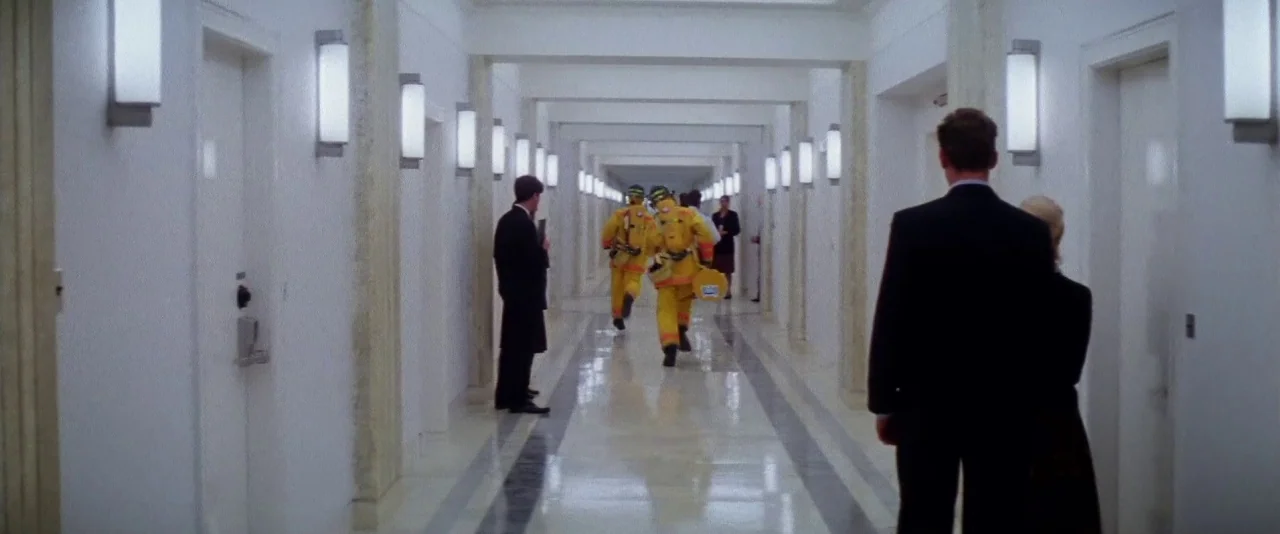 Mission: Impossible (1996) movie still: wide — A sterile, modern corridor with white doors and polished floors stretches into the distance. Several…