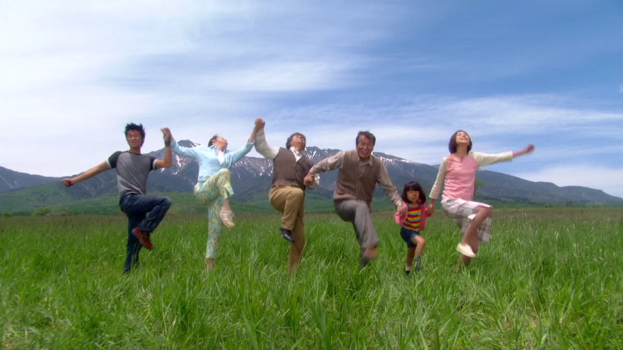 The Happiness of the Katakuris (2001) movie still: fullbody — A group of six people stand in a line on a vast green field. Behind them are…