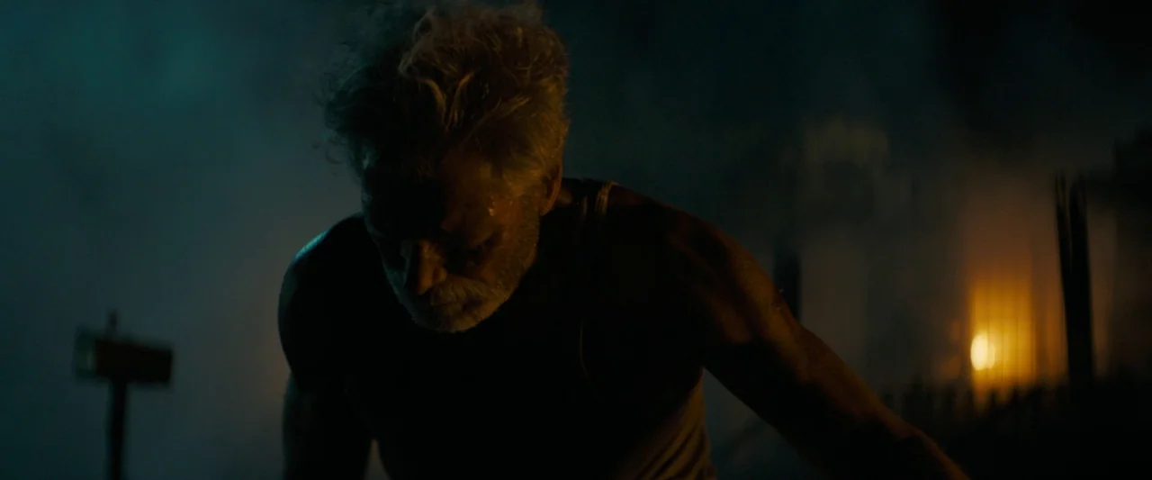 Don’t Breathe 2 (2021) movie still: medium — An outdoor night environment features an obscured, dark horizon with a distant fire glow. An older man…